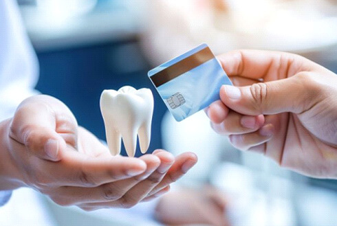 hand holding credit card ready to make exchange with hand holding tooth model