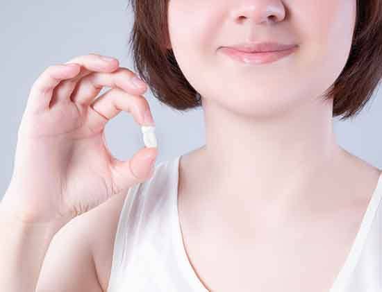 nose to chest view of a woman with short brown hair and white tank top holding her extracted tooth with 2 fingers