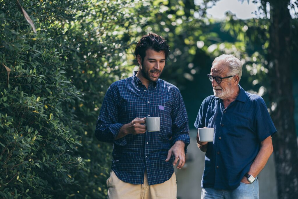 Older man in blue shirt talking to younger man in checkered shirt outside